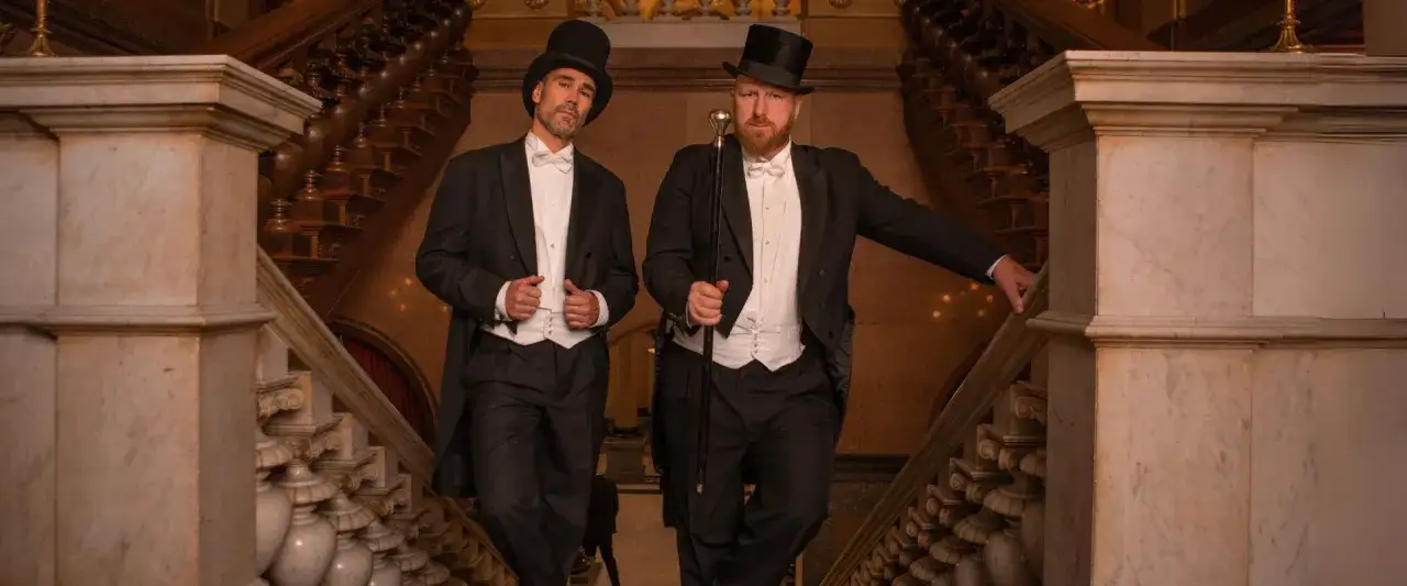 Zwei Männer in Frack und mit **white tie** stehen auf einer prunkvollen Marmortreppe.
