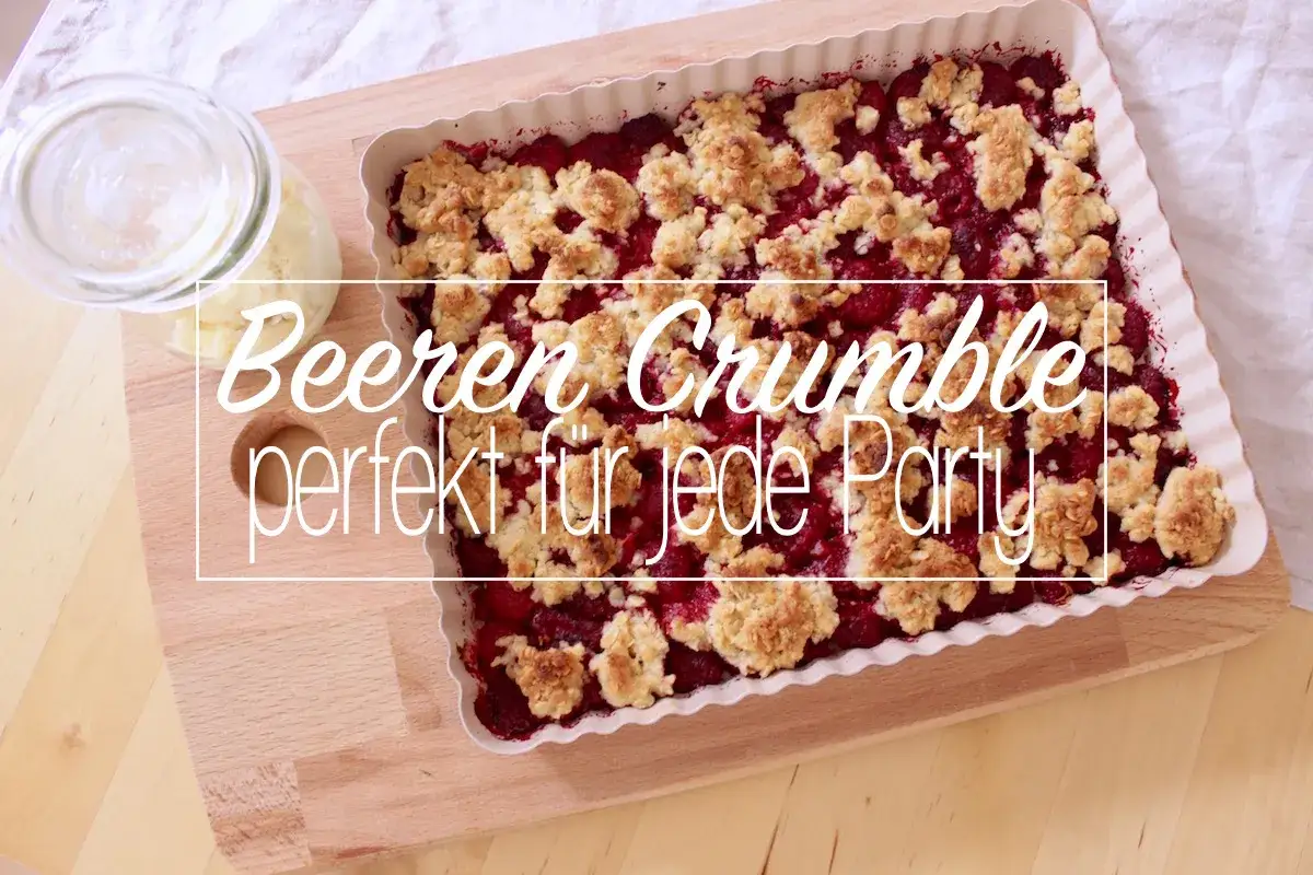 Ein frisch gebackener Beeren Crumble in einer Auflaufform, perfekt für jede Party. Daneben ein Glas mit Zutaten.