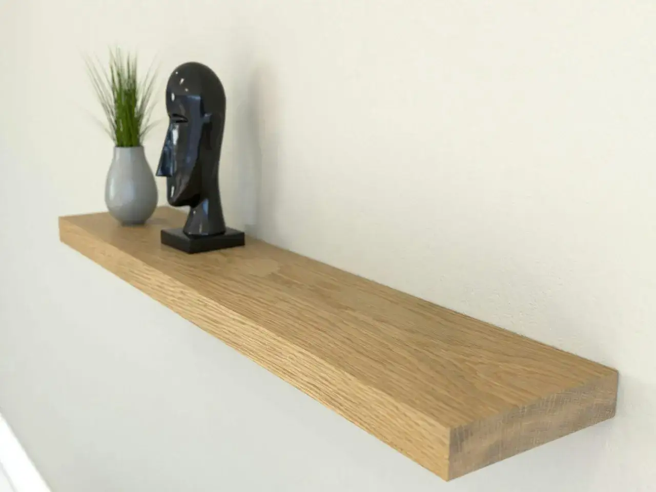 Estanter&iacute;a flotante de madera, ideal para poner baldas en pared sin escuadras. Decorada con un busto negro y una planta.