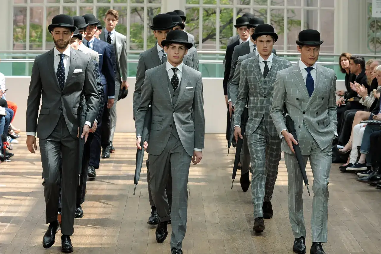 Models walk a runway, dressing formally in grey plaid suits and bowler hats.