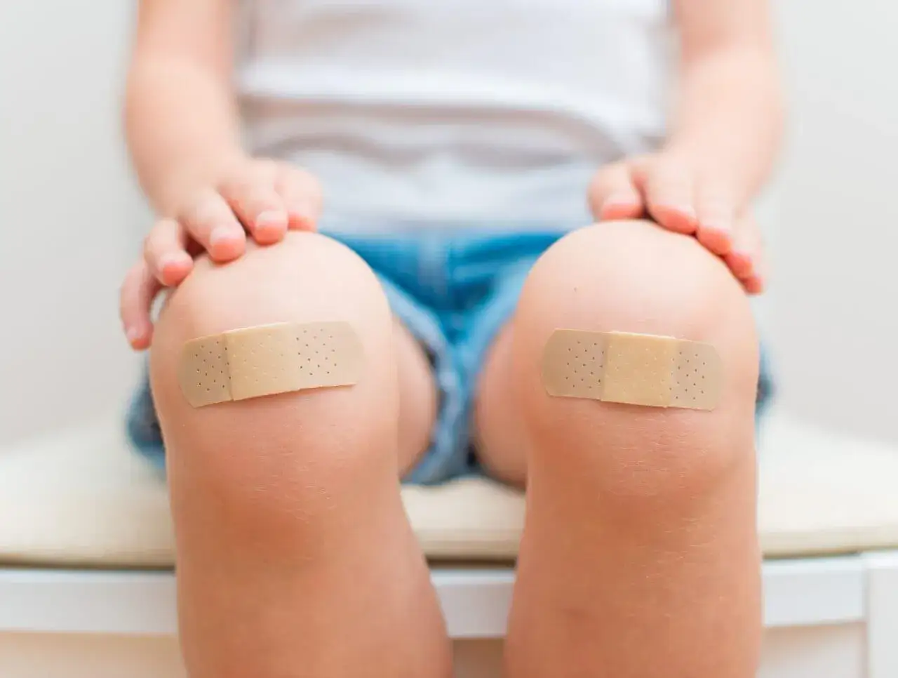 Dziecko z dwoma plasterkami na kolanach po upadku. Każde rozbite kolano zostało opatrzane.