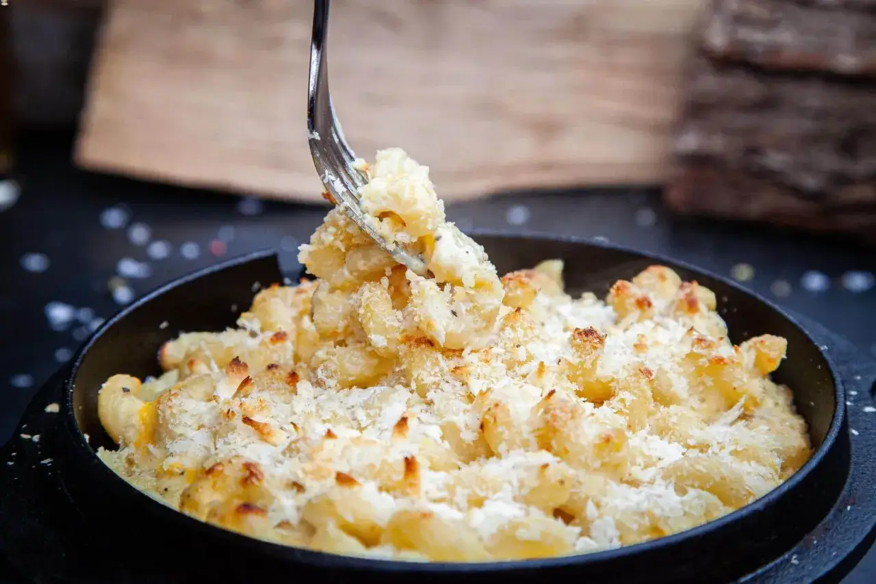 Eine Gabel hebt cremiges Mac and Cheese aus einer schwarzen Pfanne, bestreut mit knusprigen Semmelbr&ouml;seln.