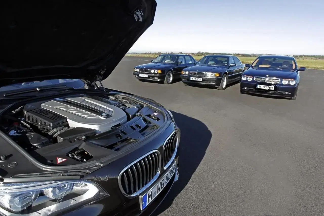 Czarny sedan BMW z otwartą maską, ukazującą potężny silnik V12. W tle trzy inne BMW.