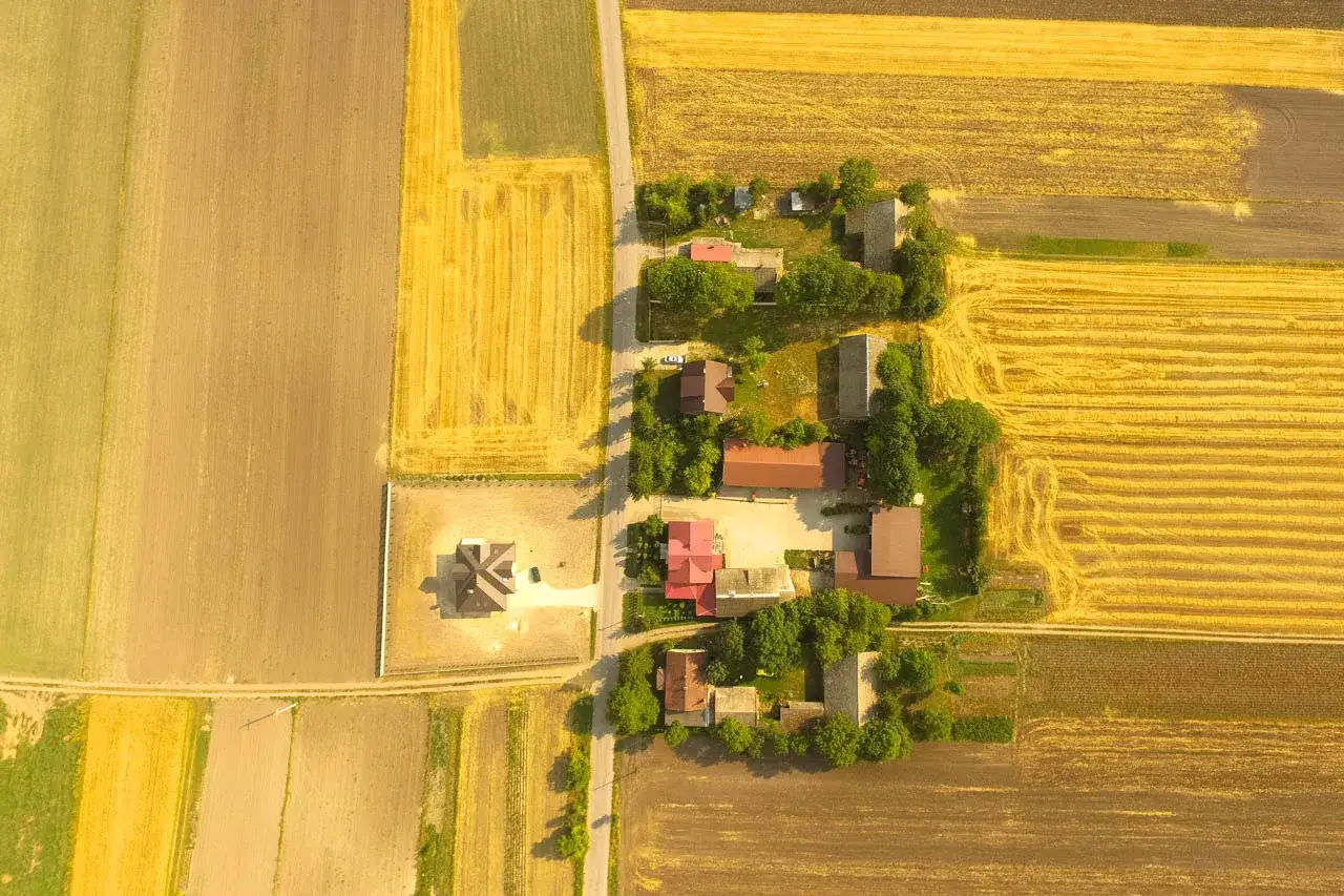 Widok z lotu ptaka na wieś z polami i domami. Sprzedaż działki z warunkami zabudowy a VAT – kluczowe informacje dla inwestorów.
