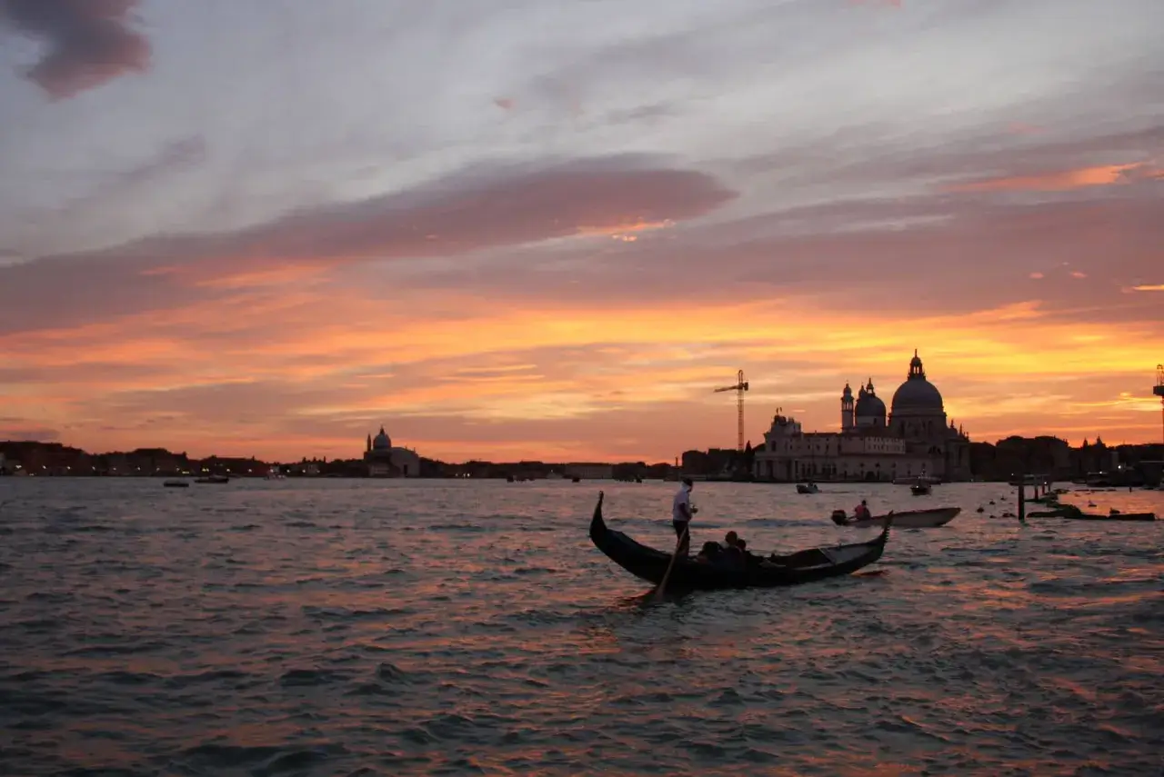 Tramonto infuocato su Venezia, citt&agrave; dell'amore, con gondole che scivolano sull'acqua e cupole maestose all'orizzonte.