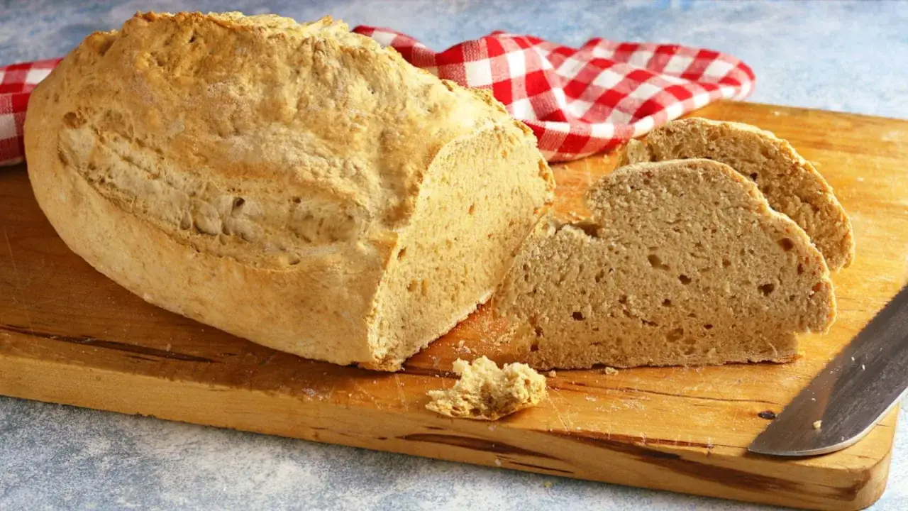 Pane rustico con lievito istantaneo, tagliato su un tagliere di legno, con un tovagliolo a quadri rossi sullo sfondo.
