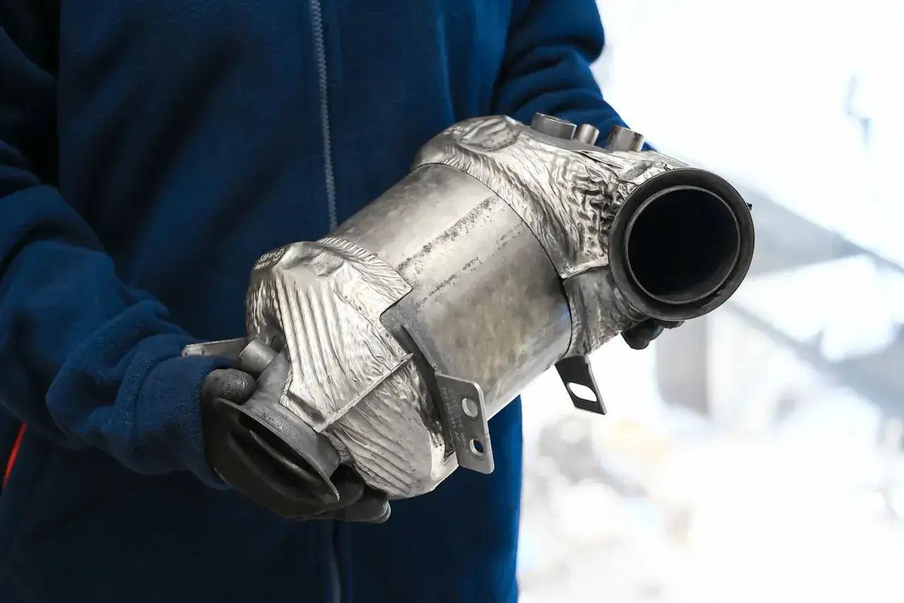 Osoba w rękawiczkach trzyma metalowy element układu wydechowego, prawdopodobnie filtr DPF.