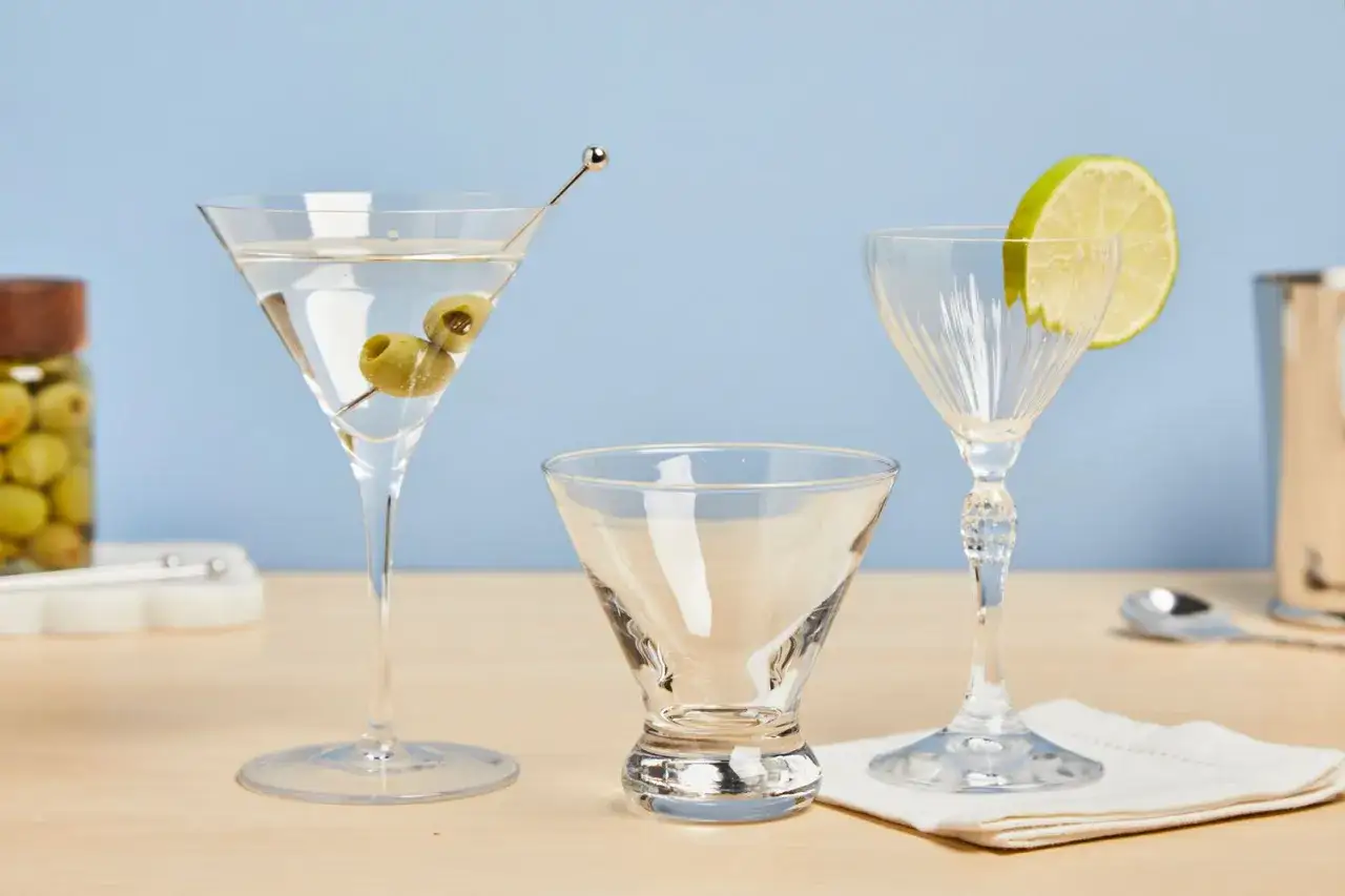 Gotowy drink z martini z oliwkami, obok puste kieliszki i plasterek limonki.