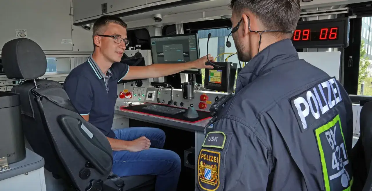 Zwei Männer im Inneren eines Polizeifahrzeugs, einer erklärt dem anderen die Technik. Ein spannender Einblick in den Polizeiberuf.