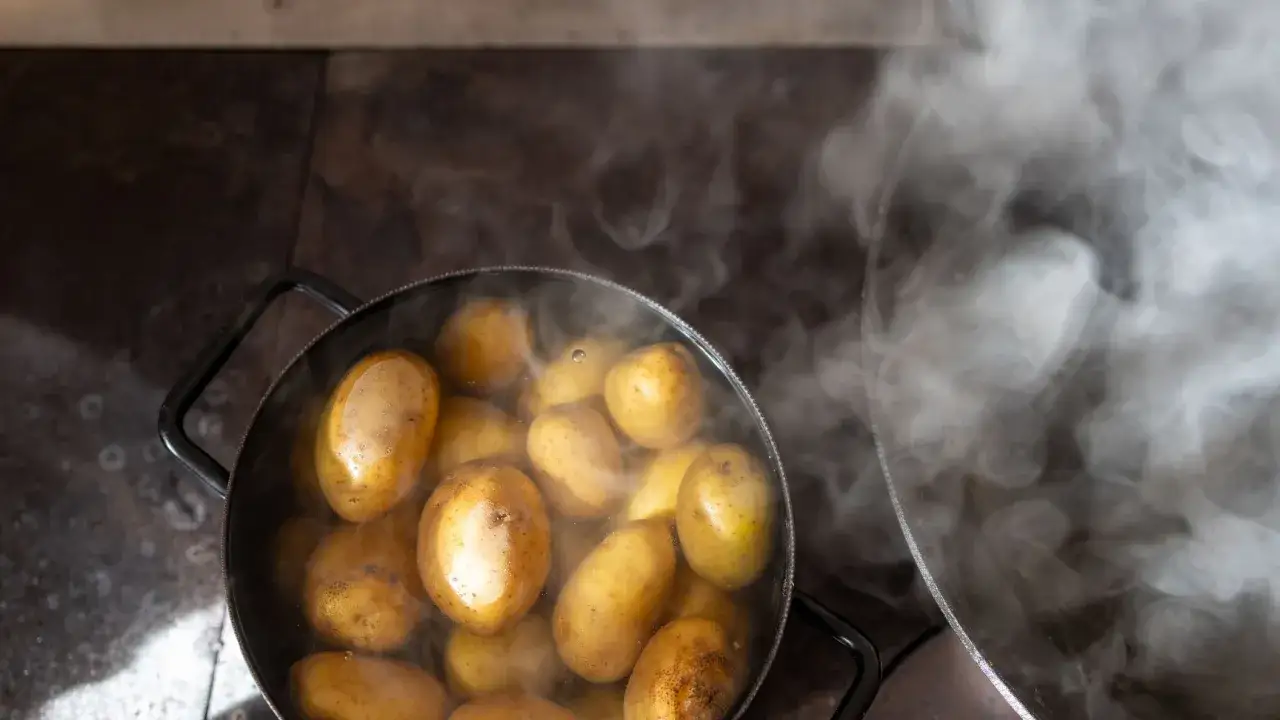 Patate intere che bollono in una pentola, emanando vapore. Il tempo di cottura delle patate lesse senza buccia è quasi terminato.