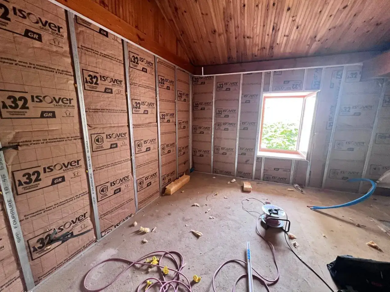 Préparation pour faire un faux plafond : murs isolés avec des panneaux Isover, structure métallique en place, fenêtre ouverte sur l'extérieur.