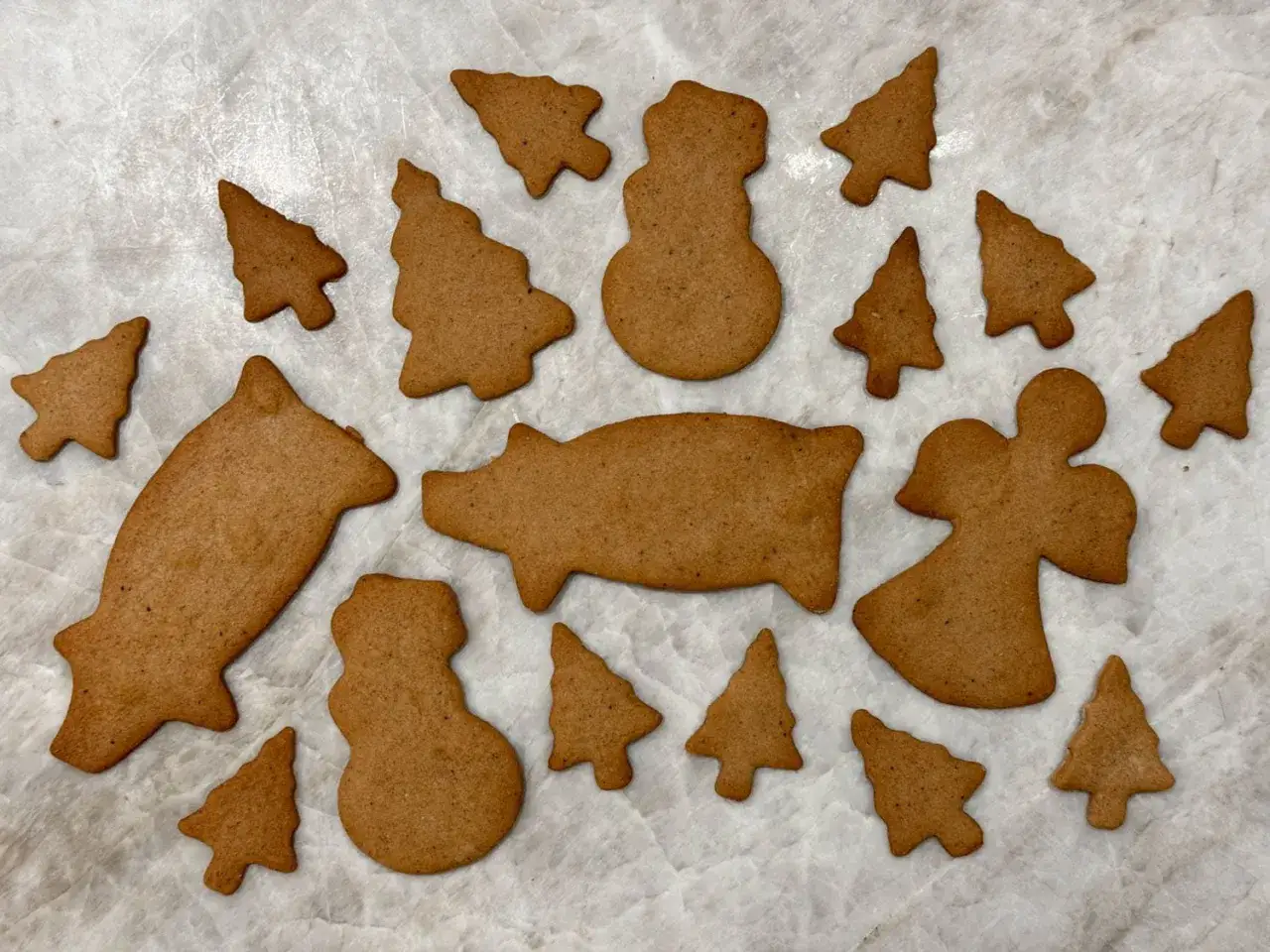 En samling skurna pepparkakor utan mandel i olika former: grisar, snögubbar, änglar och granar. Perfekta för julbaket!