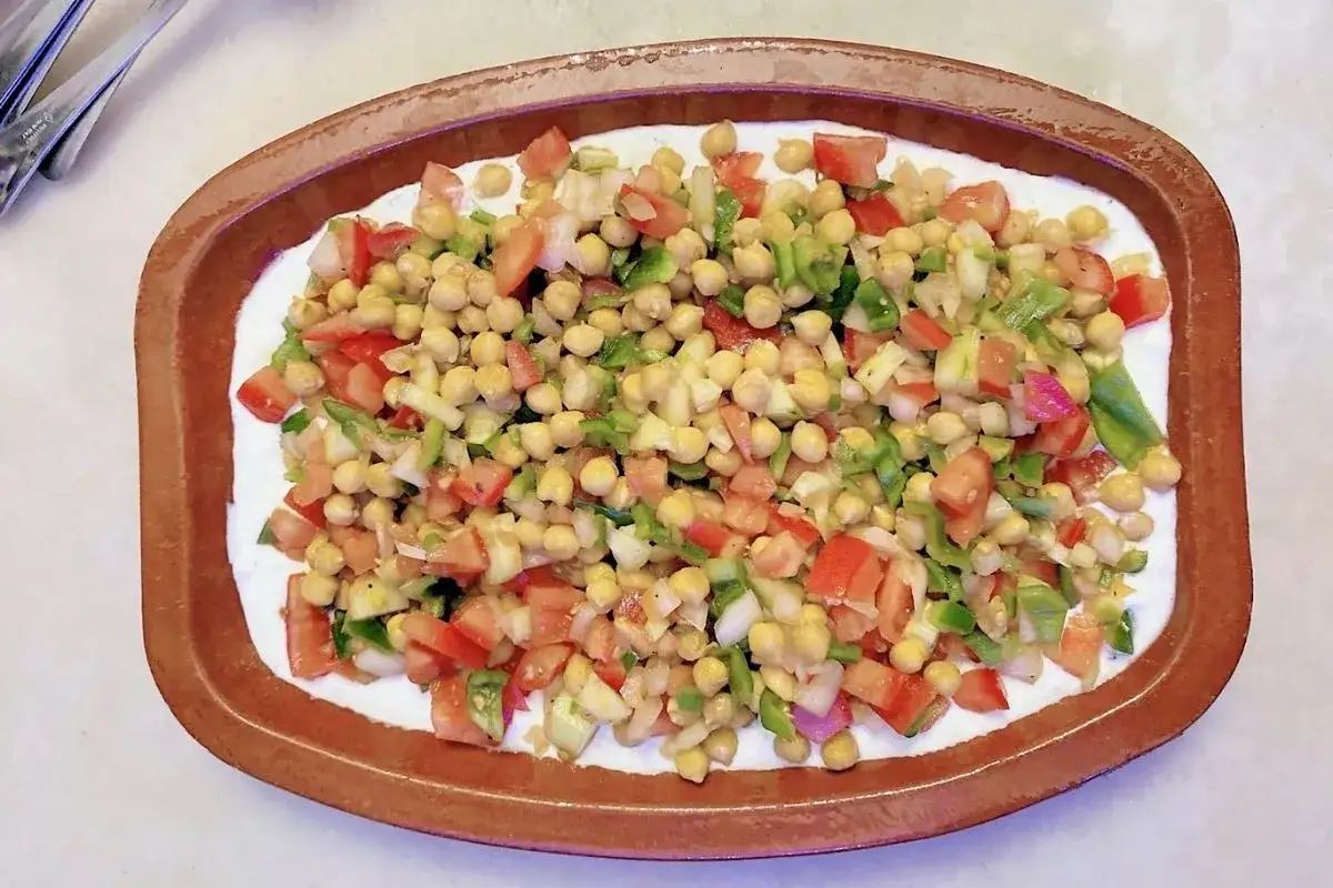 Deliciosa ensalada de garbanzos con tomate, pimiento verde y cebolla, servida sobre una base cremosa en una cazuela de barro.