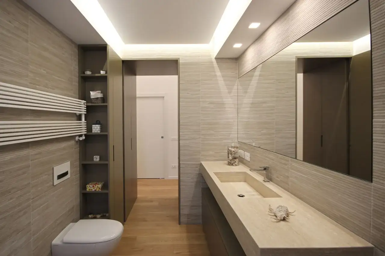 Bagno moderno con lavabo integrato, specchio ampio e un pratico antibagno senza porta che conduce a un'altra stanza.