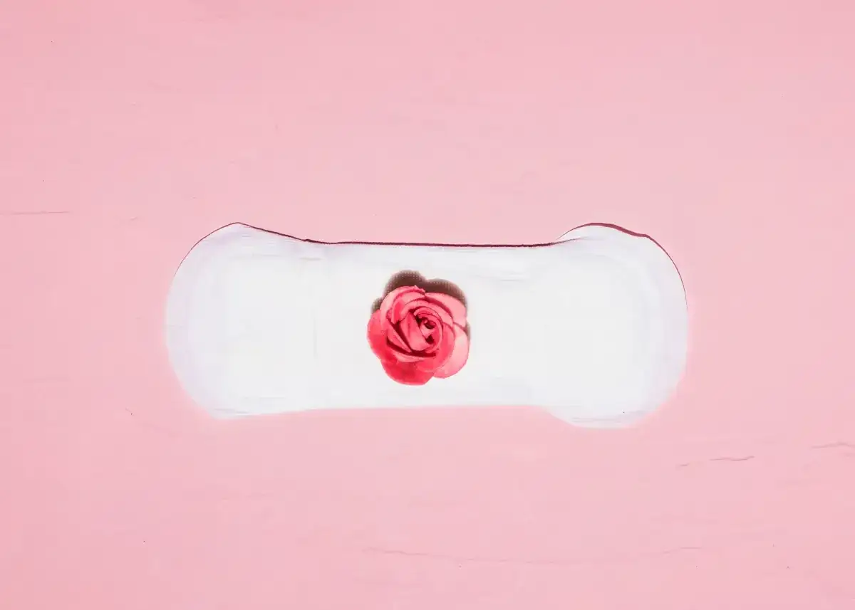 Delikatne krwawienie implantacyjne, symbolizujące początek nowego życia, na tle różowej tekstury z różą.