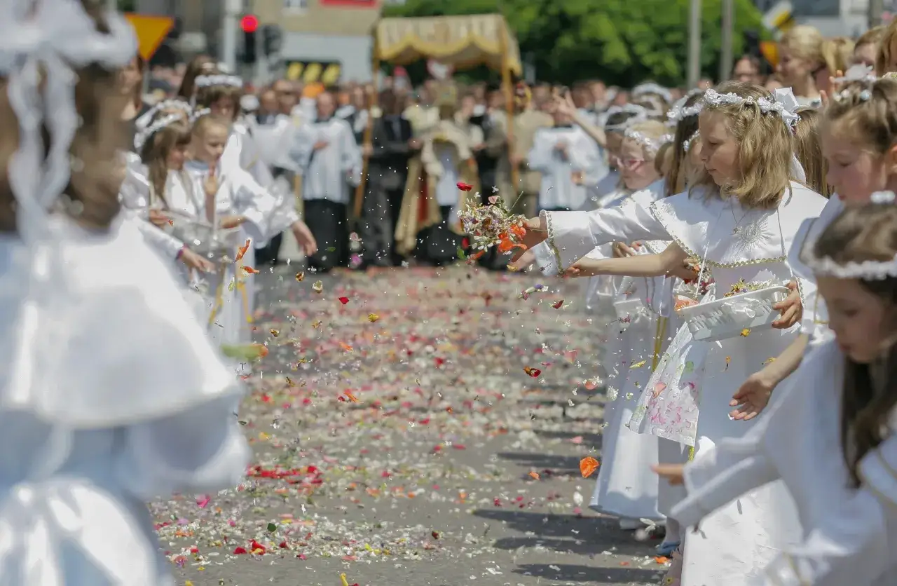 Dzieci w bieli sypią kwiaty na procesję Bożego Ciała.
