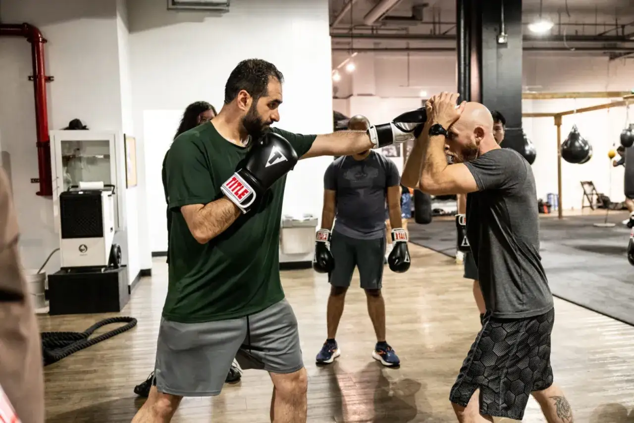 Two men in a boxing gym practice defense and offense, demonstrating sparring tips.