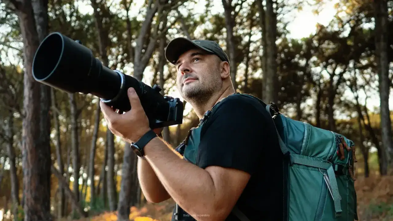 Fotografo con un teleobiettivo, pronto a catturare la natura. Il suo zaino &egrave; un om system, perfetto per le avventure.