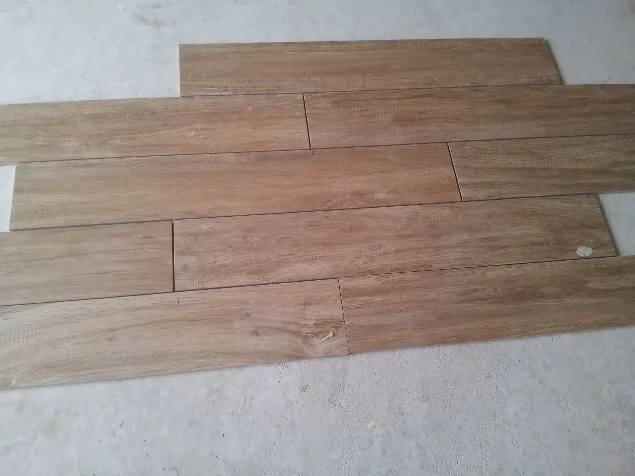 Pose de carrelage imitation parquet en cours. Les lames de bois clair sont posées sur un sol brut.