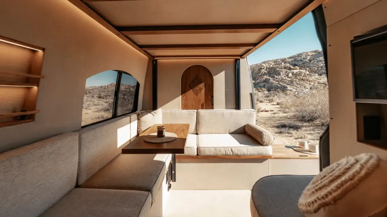 Am&eacute;nagement int&eacute;rieur d'un van : banquettes confortables, table en bois, et vue sur le d&eacute;sert. Une invitation au voyage avec une d&eacute;co interieur van chaleureuse.
