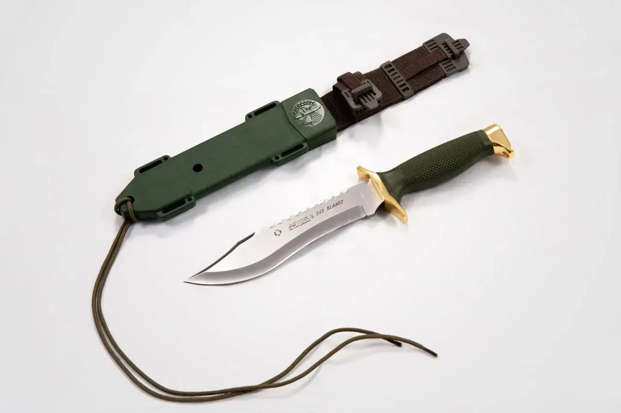 Cuchillo Aitor con funda verde y cord&oacute;n. La hoja del cuchillo oso blanco tiene un filo dentado y un protector dorado.