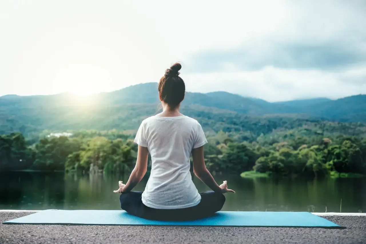 Mujer meditando junto a un lago, practicando los principios del yoga en un entorno natural sereno.