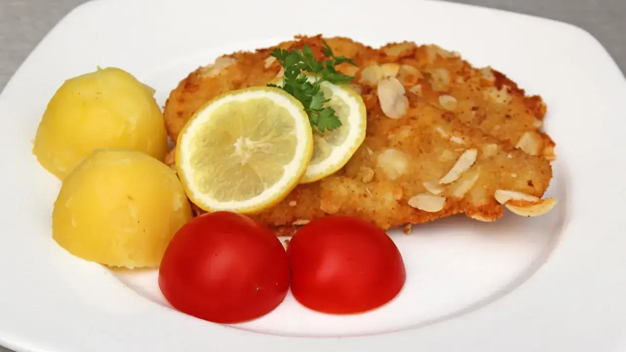 Knuspriges low carb putenschnitzel mit Mandeln, garniert mit Zitronenscheiben und Petersilie, serviert mit Salzkartoffeln und Tomaten.