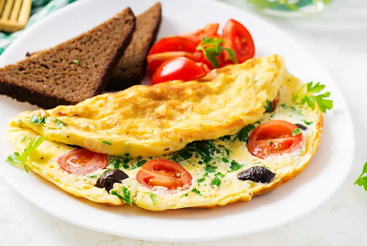 Omlet z pomidorami i oliwkami, podany z ciemnym pieczywem. Idealne lekkostrawna kolacja przepisy na zdrowy posiłek.