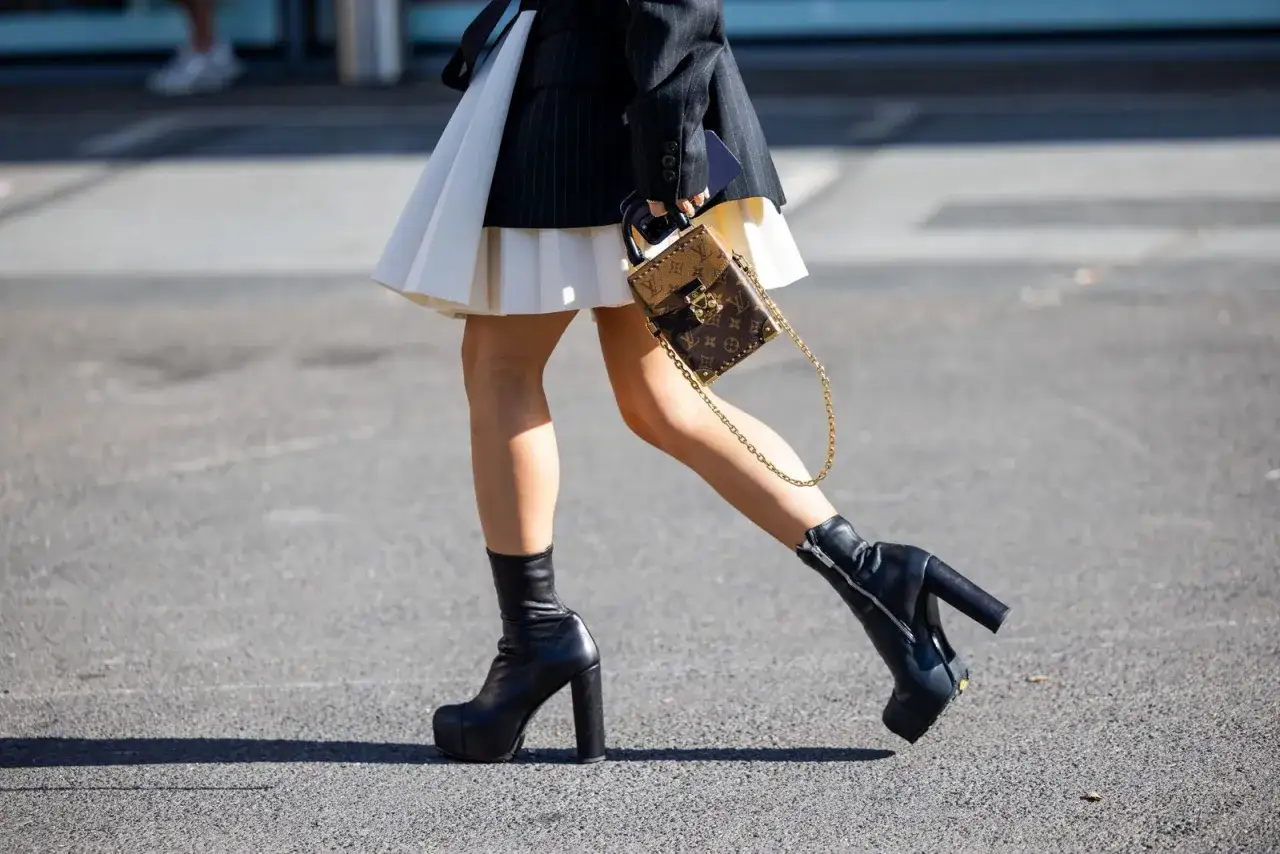 Estilos de botines: botines negros con plataforma y tac&oacute;n grueso, combinados con falda plisada y bolso de dise&ntilde;ador.