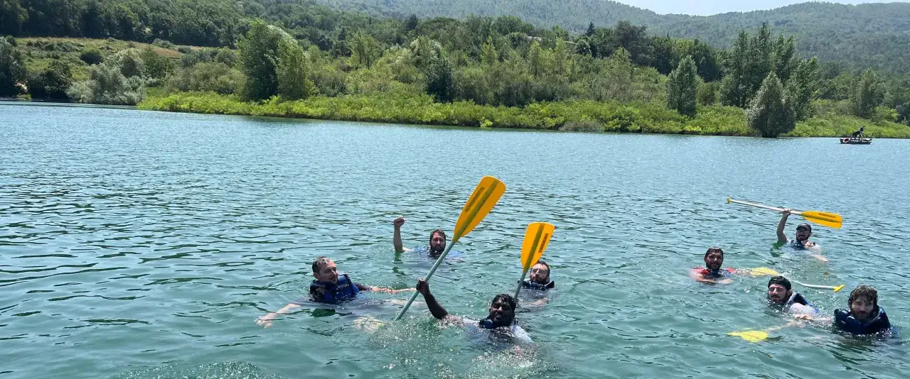 Un gruppo di amici si diverte nel lago di Bilancino, alcuni con giubbotti salvagente, altri con pagaie gialle, in una giornata di sole.