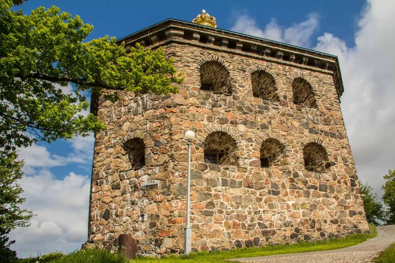 Skansens torn i Haga, Göteborg, med sin stenmur och gyllene krona, reser sig mot en blå himmel med moln.