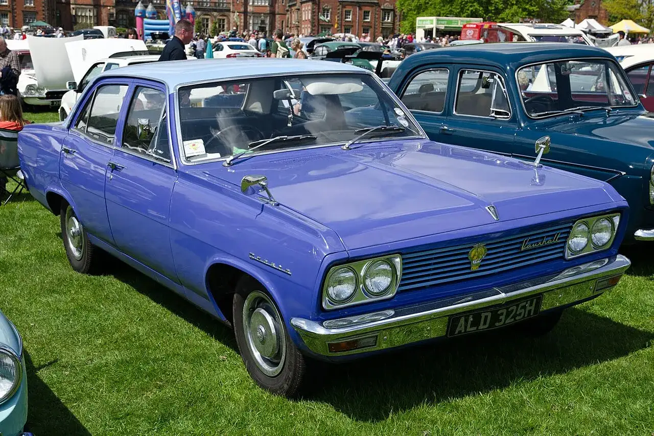 En lila Vauxhall Cresta fr&aring;n 1960-talet st&aring;r p&aring; en gr&auml;smatta, bredvid en m&ouml;rkbl&aring; bil.