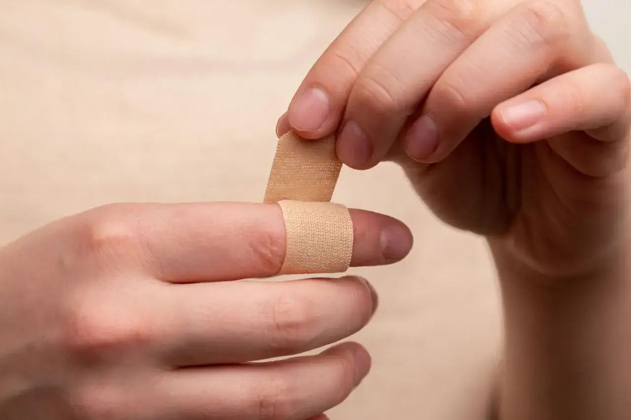 Dłoń zakłada plaster na palec, chroniąc go przed zranieniem. To proste rozwiązanie, gdy coś na ziarninie wymaga opatrunku.