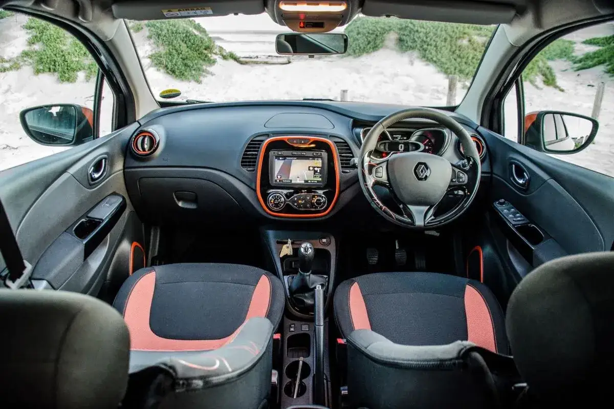 Wnętrze Renault Captur 2016 z pomarańczowymi akcentami, ekranem nawigacji i dwukolorowymi siedzeniami.