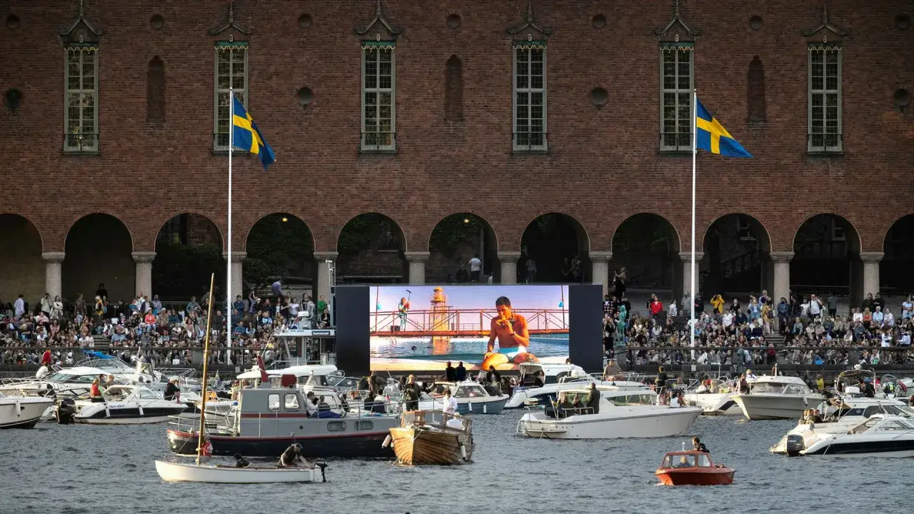 Storbildsskärm visar en scen vid vattnet i waterfront Stockholm. Många båtar ligger förtöjda.