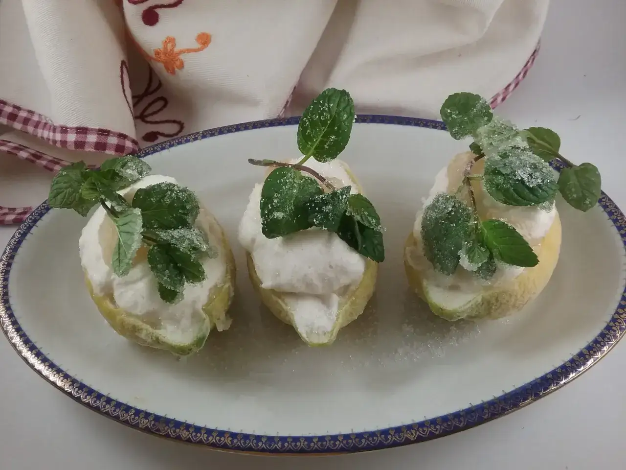 Tre limoni svuotati, ripieni di soffice mousse al limone e decorati con menta e zucchero a velo.