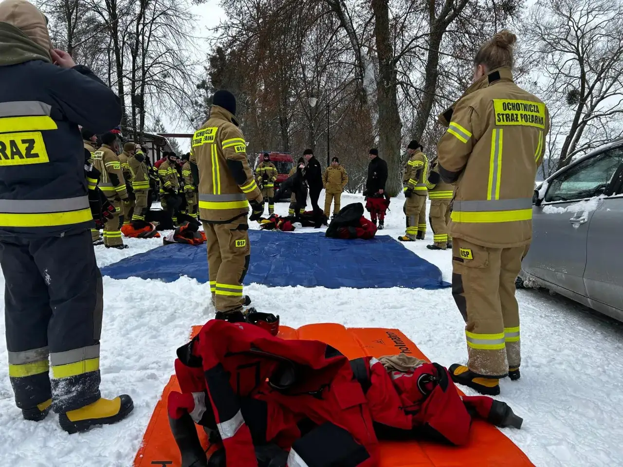 Drużyna KSRG OSP w akcji zimowej. Strażacy w mundurach przygotowują sprzęt na śniegu.