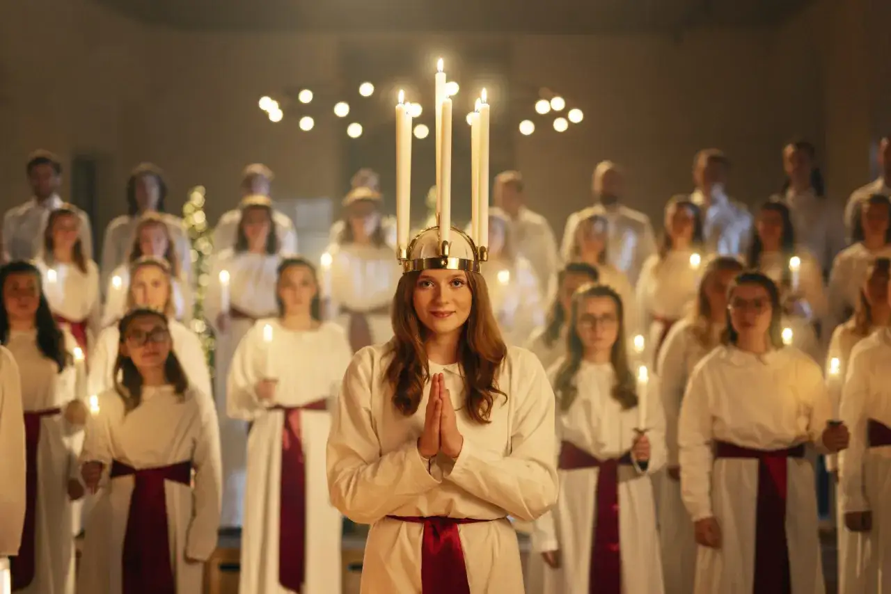 En Lucia med ljus i håret och en kör av vita kläder och ljus. Namnet Lucia betyder ljus, vilket passar denna stämningsfulla bild.