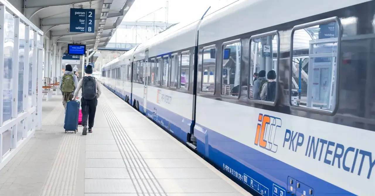 Dwaj podróżni z plecakami i walizkami idą peronem do pociągu PKP Intercity. Może jadą ze Szczecina do Łodzi?