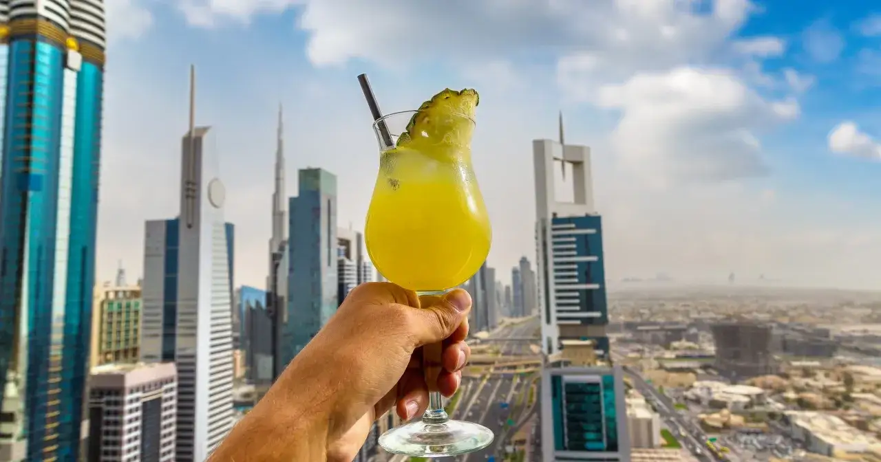 Ręka trzymająca drinka z ananasem na tle drapaczy chmur w Dubaju. Tak, w Dubaju można pić alkohol w wyznaczonych miejscach.