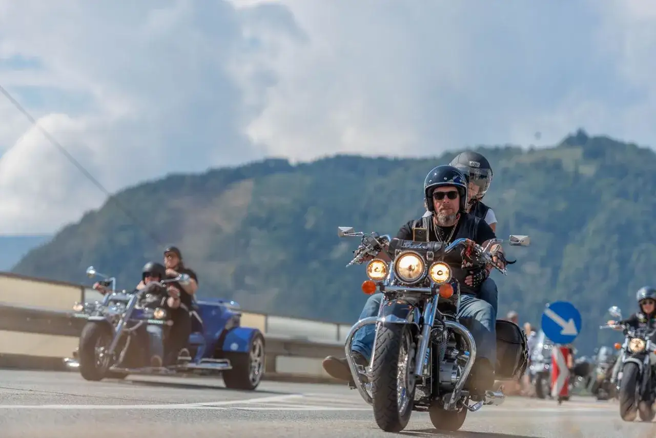 Coppia in moto durante la European Bike Week, con un trike blu e altre moto sullo sfondo.