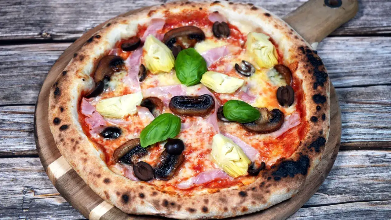 Pyszna pizza capricciosa z szynką, pieczarkami, karczochami i oliwkami, udekorowana listkami bazylii.