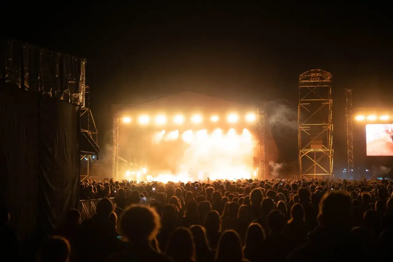 Tłum ludzi na nocnym koncercie, rozświetlonym sceną i dymem. Niezapomniany wieczór na **summer punch festival**.