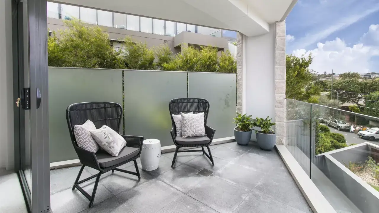 Un terrazzo sul tetto con due sedie, un tavolino e piante, offre una vista su un quartiere alberato.