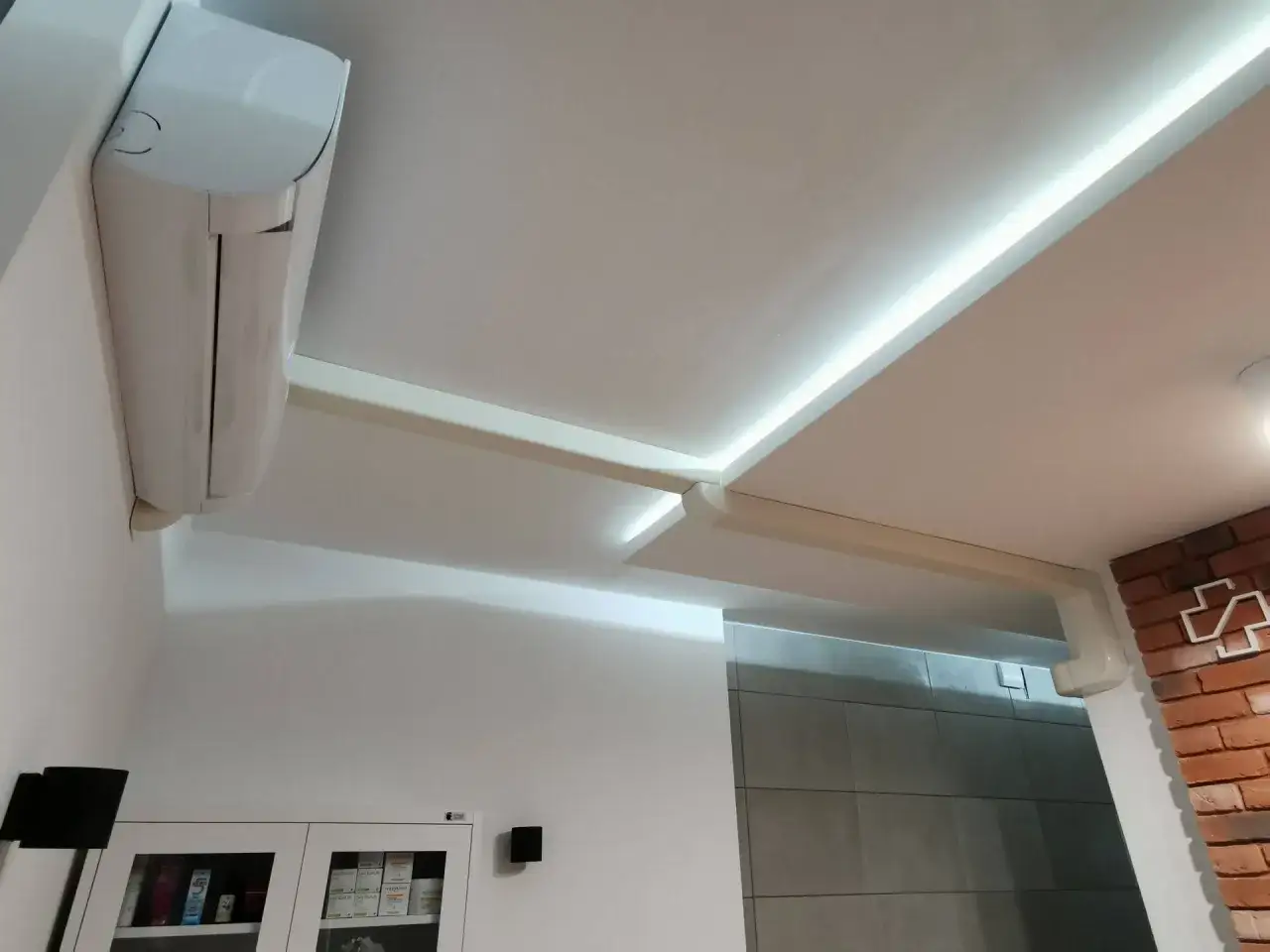 Biała jednostka klimatyzacyjna zamontowana na ścianie pod sufitem z podświetleniem LED.