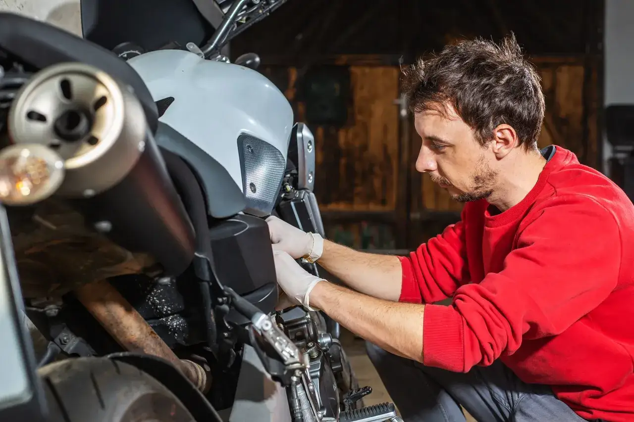 Uomo con guanti bianchi lavora su una moto in un garage.