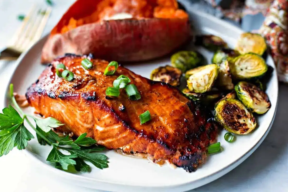 Filet de saumon glacé, prêt pour un barbecue, servi avec une patate douce et des choux de Bruxelles rôtis.