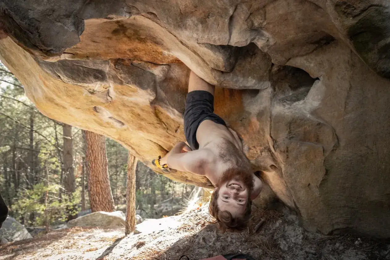 Ein Kletterer h&auml;ngt kopf&uuml;ber an einem beeindruckenden Fontainebleau Boulder.
