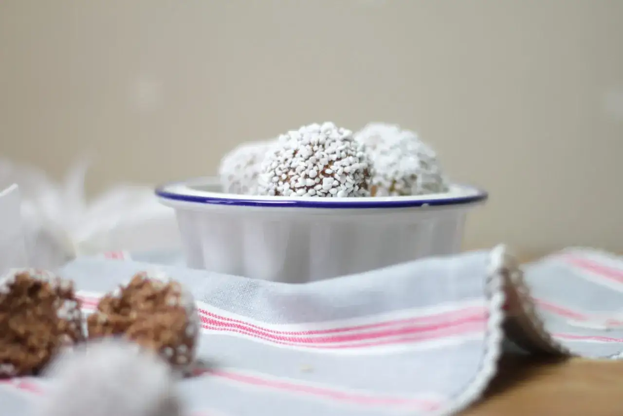 Små, rullade havrebollar med kokosflingor i en vit skål. Ett enkelt havrebollar recept för fikat.