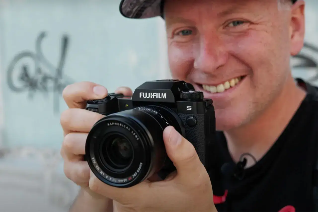 Uśmiechnięty mężczyzna trzyma aparat Fujifilm XH2S z obiektywem.